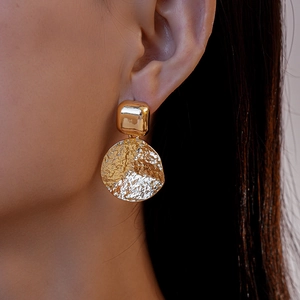 Vue macro de boucles d'oreilles dorées avec clous carrés et disques à texture martelée