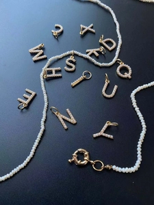 Vue macro de breloques alphabet dorées avec perles sur un fond texturé bleu marine