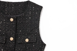Close-up of black tweed vest featuring golden twisted buttons and sparkling sequins