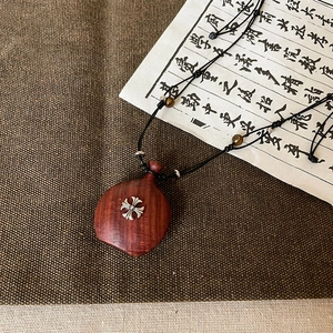 Détail macro du pendentif cœur en bois avec croix en métal et perles d'œil de tigre
