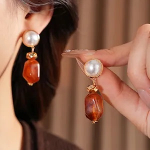 Vintage pearl earrings with irregular translucent orange resin drops on brown background
