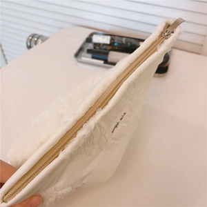 Detail of white quilted lace cosmetic bag featuring metal zipper and side embroidery
