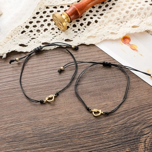 Detail of adjustable couple bracelets with golden heart knots on a black woven cord