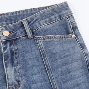 Détail macro du jean évasé bleu avec bouton doré, poche avant et texture de denim