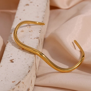 Macro shot of minimalist gold wave-shaped open bangle on textured stone with silk fabric