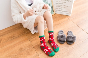 Close-up of warm Christmas elk coral fleece socks worn on cozy wooden floor for winter