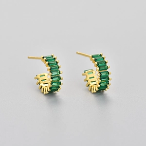 Macro view of gold C-shaped earrings featuring emerald baguette-cut cubic zirconia