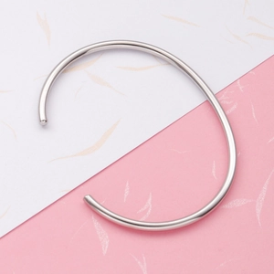 Minimalist silver stainless steel C-shaped open bangle shown on a textured pastel background