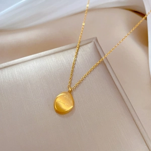 Close-up of golden irregular bean pendant with brushed metal texture on silk background