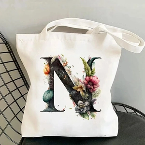 Detail view of white canvas tote bag featuring floral letter N print and shoulder strap