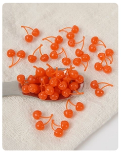 Miniature orange double cherries resin accessories on white linen with a metal spoon