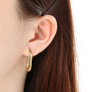 Close-up of elegant oval 18k gold plated stainless steel U-shape hoop earring worn by model