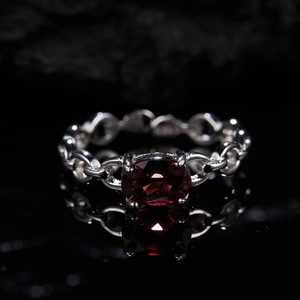 Macro shot of silver chain ring featuring a large oval deep red garnet on a black surface