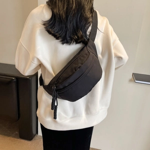 Dettaglio di una borsa a tracolla in nylon nero indossata come marsupio alla moda su modella