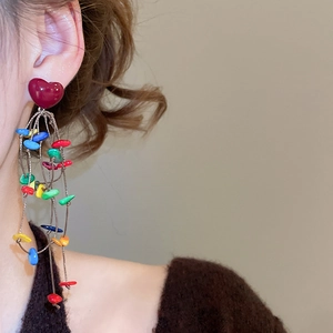 Detail of bohemian tassel earrings featuring red heart studs and colorful beads on a model