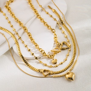 Detailed view of layered gold heart necklaces arranged on a white stone background