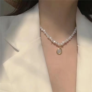 Close-up of pearl necklace with a gold-bordered gemstone pendant on a white suit
