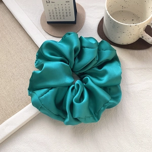 Detail showing oversized turquoise satin scrunchie with soft silk folds on a white background