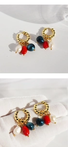 Detail of twisted gold earrings with pearl, red stone, and blue bead tassels on a hand