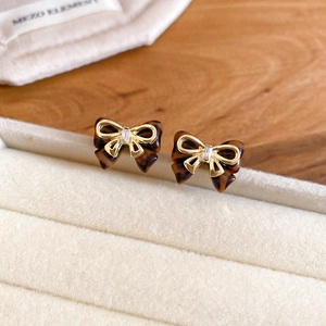 Detail of bow-shaped stud earrings with tortoiseshell texture and gold-tone metal frame