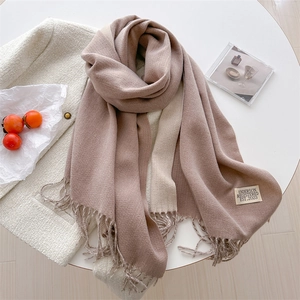Detail of soft cashmere-feel scarf with fringes and logo label on a white table