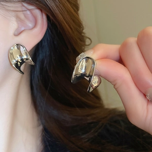 Close-up of silver C-shaped earrings with irregular liquid metal texture and glossy finish
