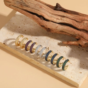 Detail of colorful cubic zirconia ear cuffs in gold and silver on a stone surface