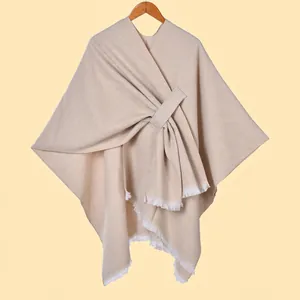 Detail of beige knit shawl featuring thick warm fabric and white fringe trim edges