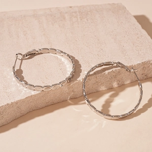 Close-up of silver oval hoop earrings with textured bamboo design on natural stone
