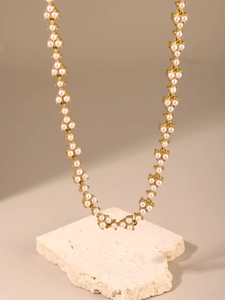 Golden chain necklace with white pearls displayed on a beige stone base stand