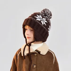 Winter knit child hat with pompom and earflaps featuring classic snowflake patterns