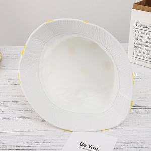 Minimalist white reversible bucket hat on wood surface with eco-friendly paper bag