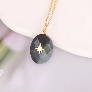 Macro shot of dark green teardrop stone pendant with gold star on stainless steel chain