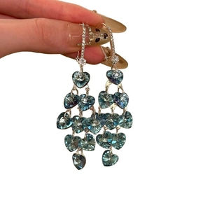 Boucles d'oreilles cœur en argent avec pompons en zircon sarcelle portées sur fond blanc pur