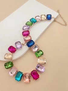 Detail of colorful rectangular crystal gems set in gold metal necklace on white pedestal