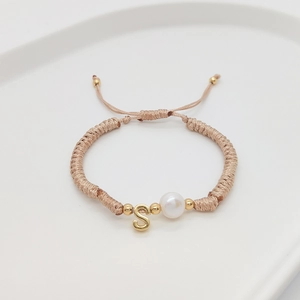 Detailed shot of handmade woven bracelet with initial S pendant and white pearl detail