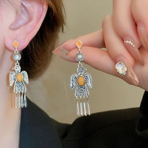 Detail of silver eagle style long earrings with orange stones on a model