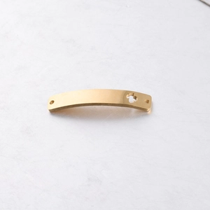 Macro detail of curved gold stainless steel rectangular connector with hollow floral pattern