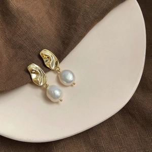 Detail of baroque pearl drop earrings featuring irregular gold metal studs and white pearls