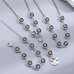 Detail of silver chain jewelry set with grey square gemstones and starburst round pendant