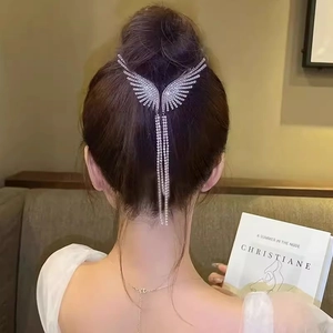 Detailed close-up of crystal angel wing hair clip with long tassel chains on a bun