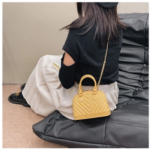 Yellow shell jelly bag with chevron quilting and golden chain strap on a black sofa