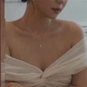 Close-up of a delicate 925 sterling silver X-shaped pendant necklace on a woman's neck