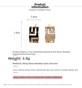 Détail de boucles d'oreilles dorées asymétriques avec émail noir et strass brillants