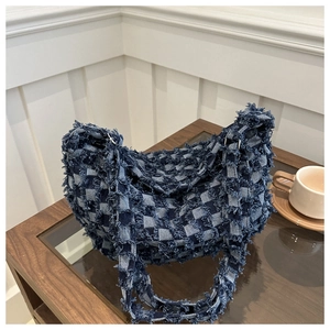 Detailed texture of blue denim checkered baguette bag with trendy frayed fringe edges