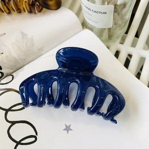 Detail view of a large navy blue high-gloss hair claw clip on a white magazine background