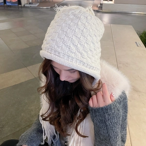 Detail of white chunky knit beanie with diamond pattern and top tassel decoration