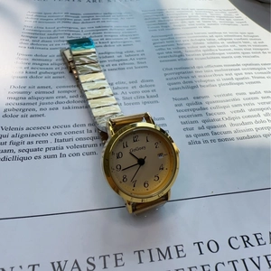 Detail view of gold quartz watch with numeric markers, calendar dial, and metal strap