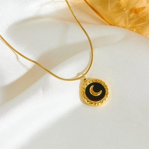 Detail of gold necklace featuring a black circular pendant with a gold moon motif on silk