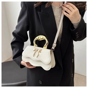 Detail view of white wave handbag with metallic bow accent and gold handle